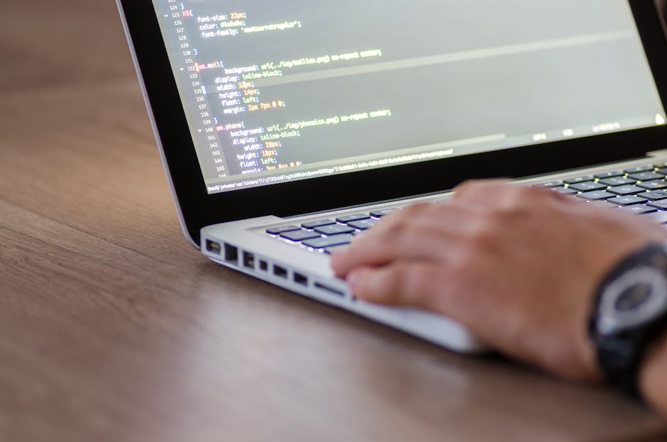 A close-up view of a laptop computer on a wooden desk, displaying lines of code in a dark-themed Integrated Development Environment (IDE), with a ceramic coffee mug placed beside it. The mug features 